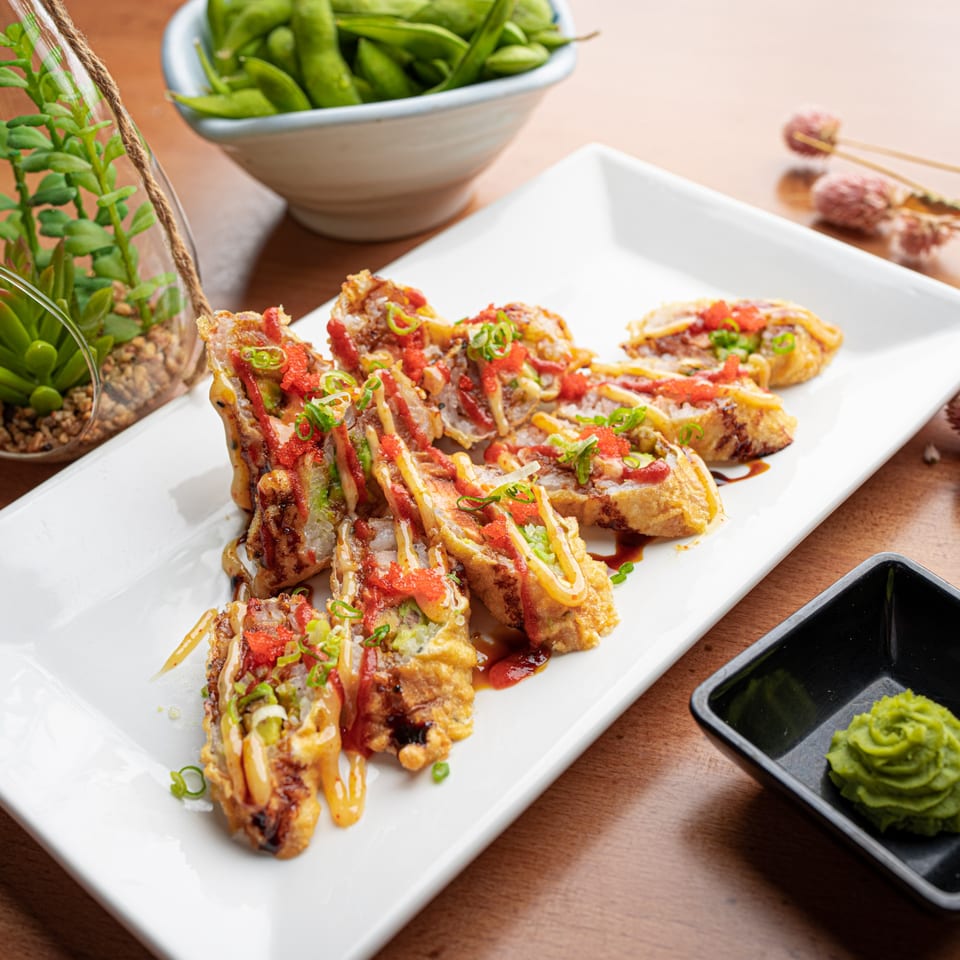 Fried sushi rolls with red and yellow sauces, green onions, and roe on a white plate.