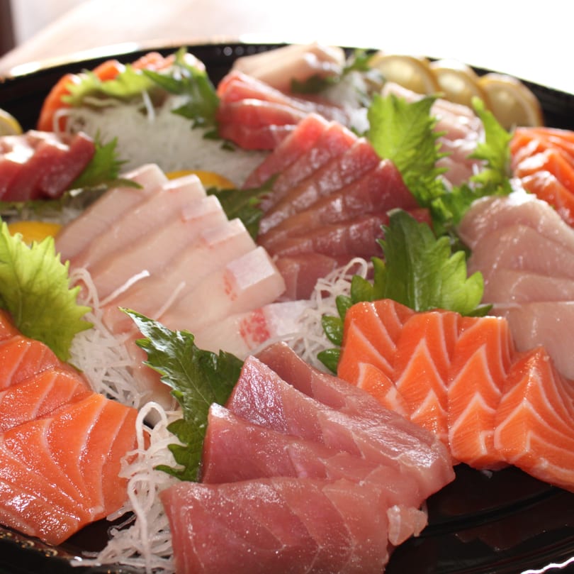 Assorted sashimi platter with salmon, tuna, and white fish, garnished with shiso leaves and daikon.