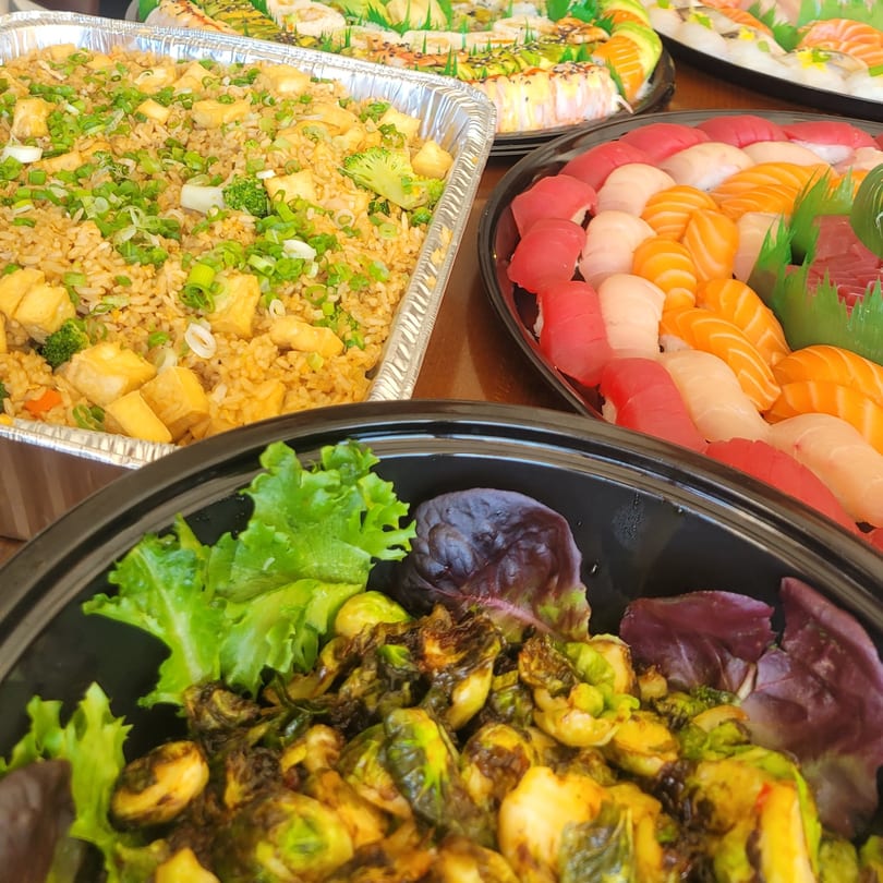 A catering spread with fried rice, sushi platters, and roasted Brussels sprouts with lettuce.