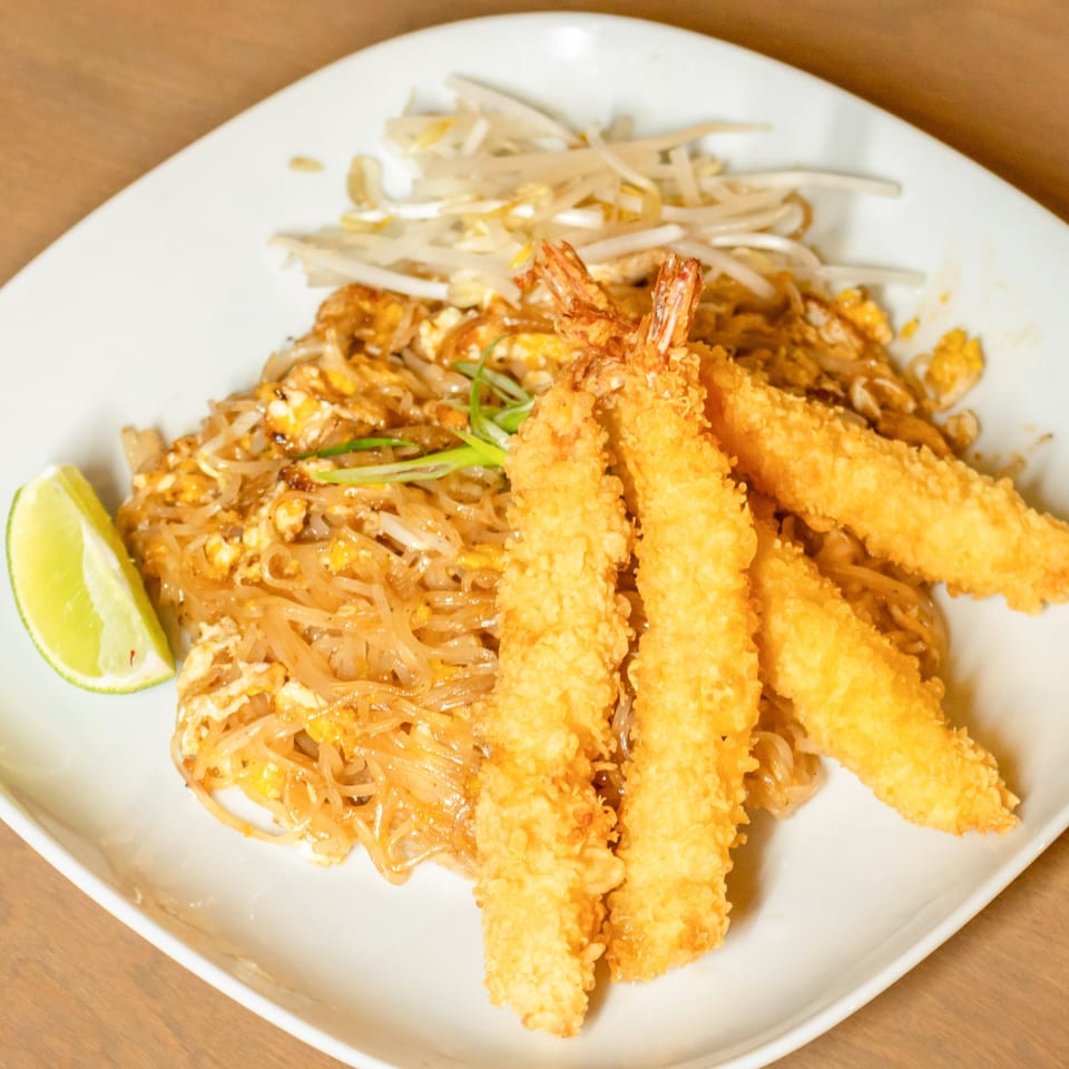 Pad Thai noodles with scrambled egg, bean sprouts, fried shrimp, and a lime wedge on a white plate.