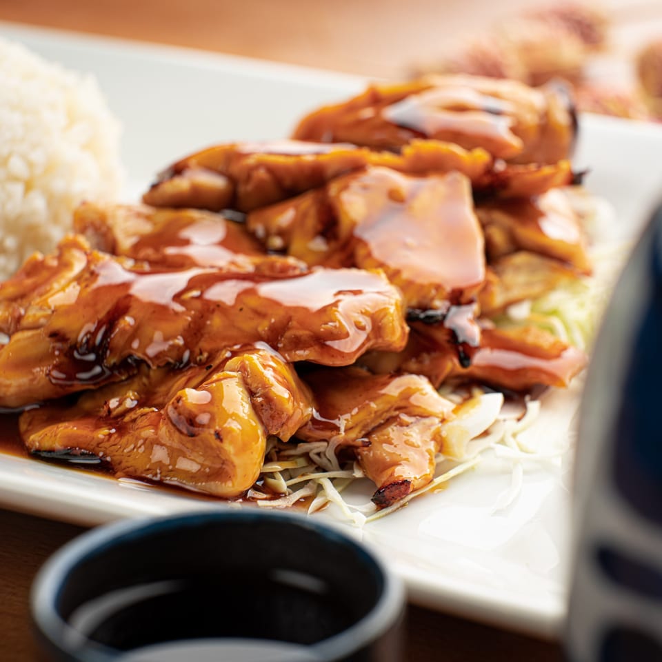 Teriyaki chicken with white rice and shredded cabbage on a white rectangular plate.