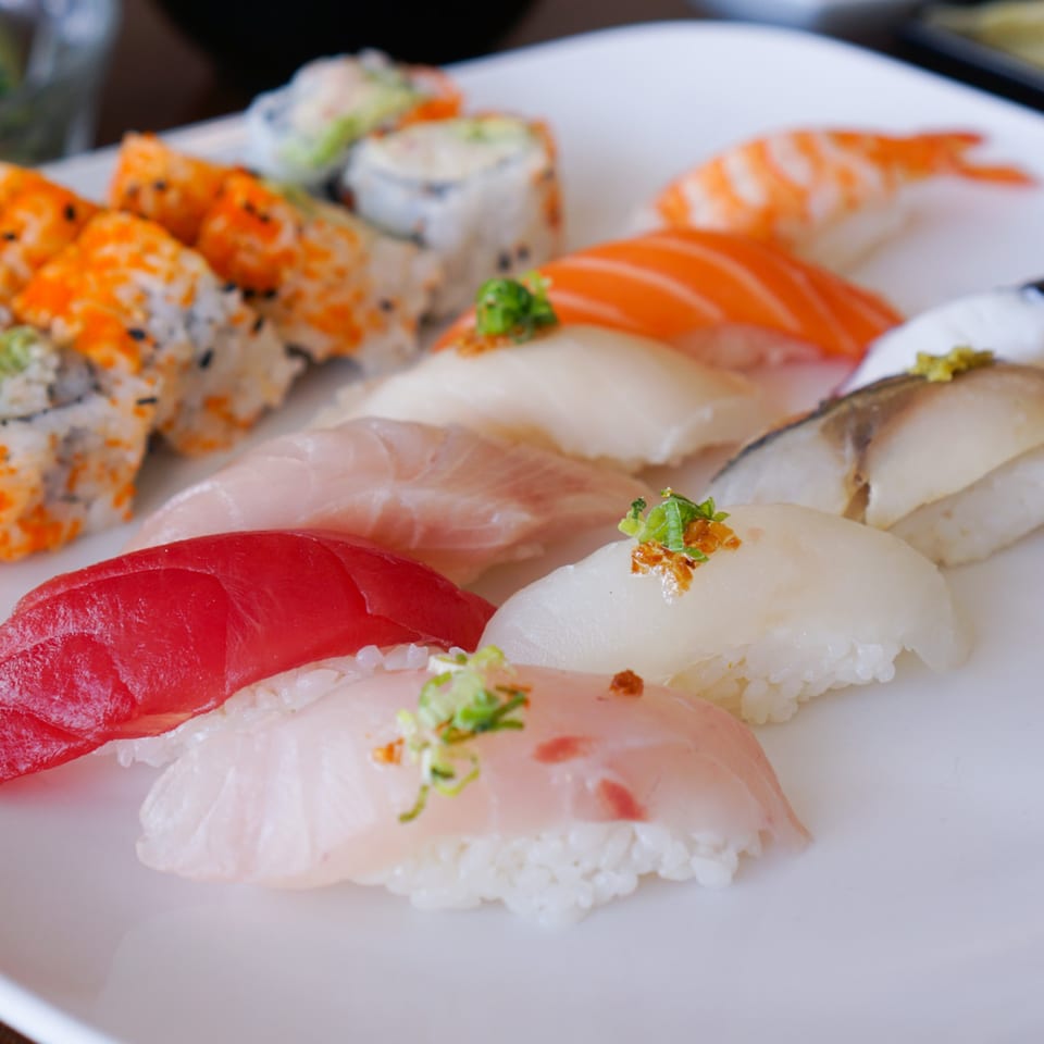 A white plate filled with various colorful sushi rolls and nigiri, including tuna, salmon, and shrimp.