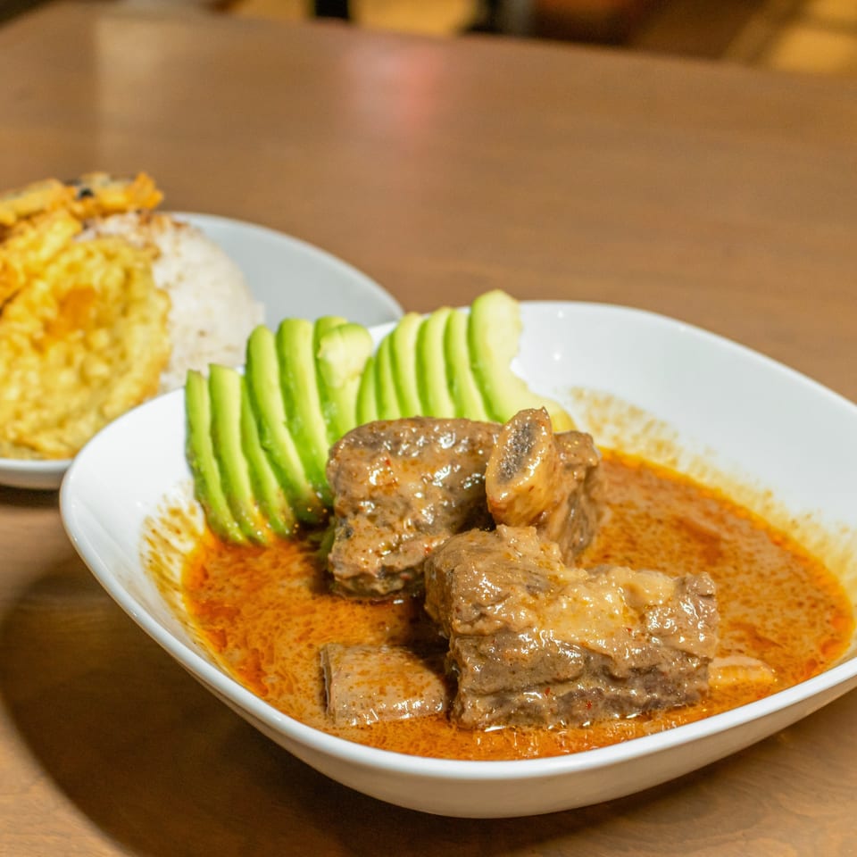 Beef stew with avocado slices and a side of rice with fried plantains.
