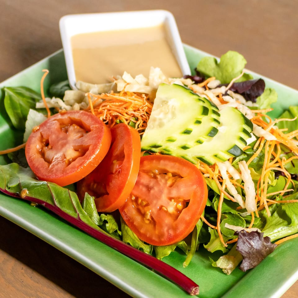 A fresh garden salad with sliced tomatoes, cucumbers, shredded carrots, and dressing on a green plate.