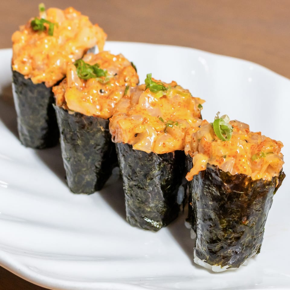 Four gunkan maki sushi pieces with spicy orange topping and green onions on a white plate.