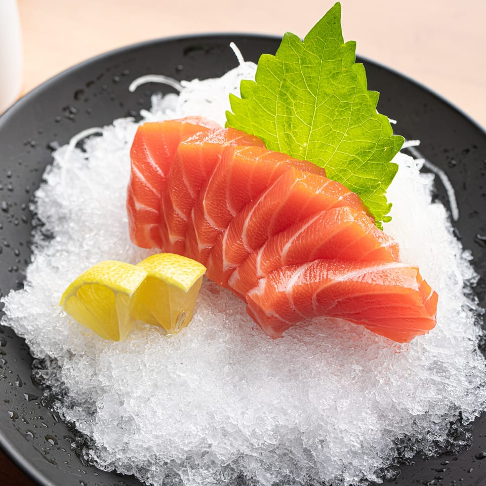 Fresh salmon sashimi slices with lemon wedges and a green leaf on a bed of ice.