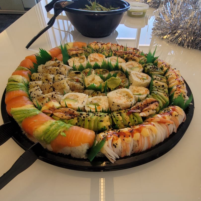 A large platter of assorted sushi rolls, including salmon, avocado, and shrimp, on a white table.