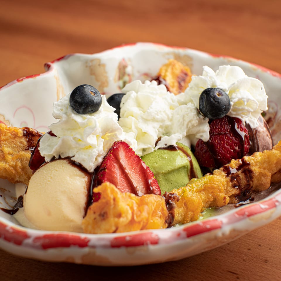 Banana split with vanilla, green tea, and chocolate ice cream, whipped cream, berries, and fried bananas.
